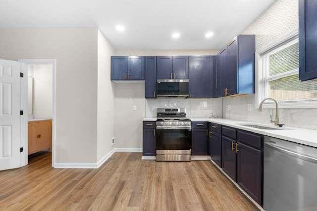 kitchen featuring blue cabinetry, sink, tasteful backsplash, appliances with stainless steel finishes, and light hardwood / wood-style floors