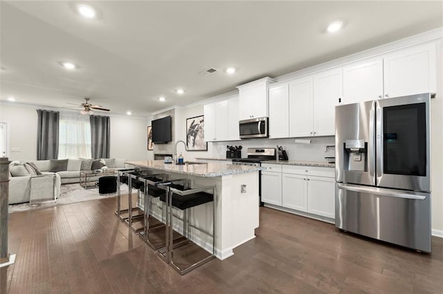 2227 Foley Park St, Snellville, GA 30078 - kitchen featuring stainless steel appliances, a kitchen island with sink, white cabinets, dark wood-style flooring, and a breakfast bar
