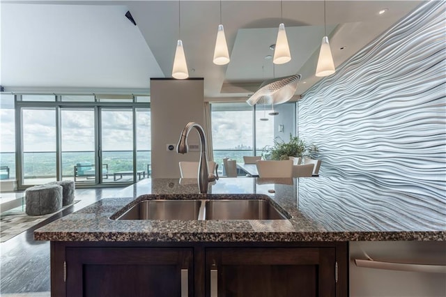 kitchen with a sink, dark brown cabinets, dark stone counters, hanging light fixtures, and expansive windows