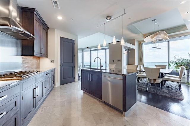 kitchen with wall chimney range hood, appliances with stainless steel finishes, a sink, dark stone countertops, and tasteful backsplash