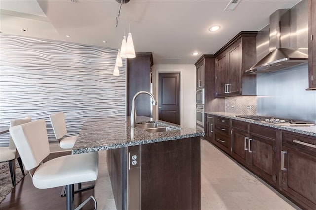 kitchen featuring wall chimney exhaust hood, a sink, appliances with stainless steel finishes, dark stone countertops, and recessed lighting