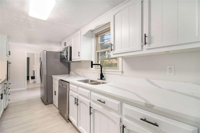 kitchen featuring sink, appliances with stainless steel finishes, light stone countertops, a textured ceiling, and white cabinets