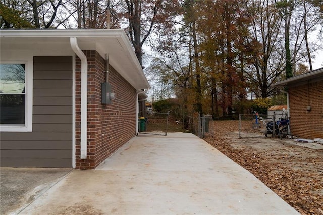 view of side of home with fence, brick siding, and a gate