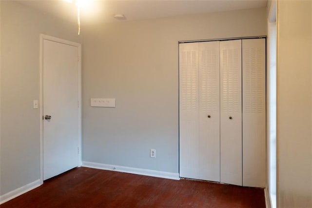 unfurnished bedroom featuring dark wood-style floors, a closet, and baseboards