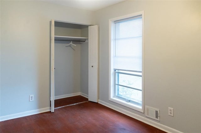 unfurnished bedroom with dark wood-type flooring, baseboards, visible vents, and a closet