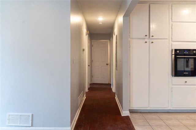 hall with visible vents, baseboards, and light tile patterned flooring