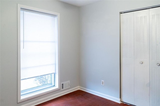 unfurnished bedroom with a closet, visible vents, dark wood-type flooring, and baseboards