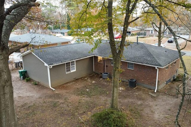 exterior space featuring brick siding, central AC unit, and roof with shingles