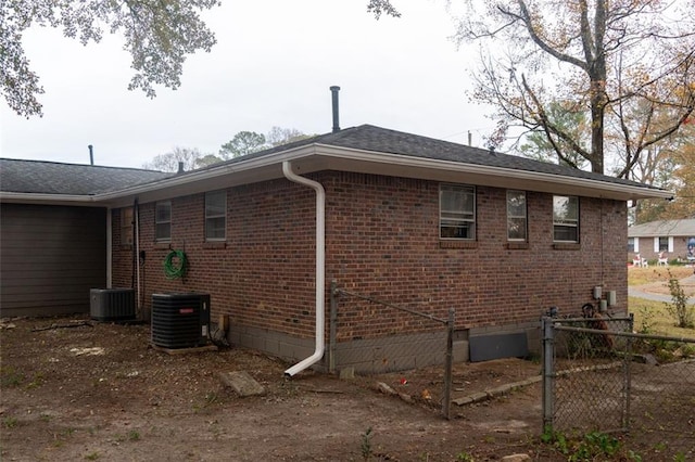 view of side of home with brick siding, cooling unit, and fence