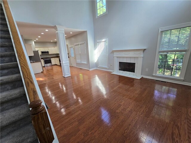 3773 Summer Rose Dr, Atlanta, GA 30341 - unfurnished living room featuring a tile fireplace, decorative columns, a high ceiling, stairs, and wood-type flooring