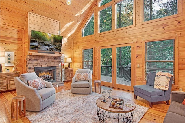 living room featuring high vaulted ceiling, hardwood / wood-style flooring, a stone fireplace, wood walls, and wood ceiling