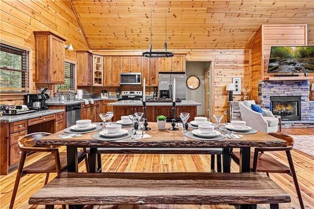 dining area with a stone fireplace, wooden ceiling, light wood-style floors, and wood walls