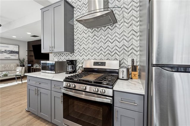 kitchen featuring gray cabinets, appliances with stainless steel finishes, range hood, light stone countertops, and light hardwood / wood-style flooring