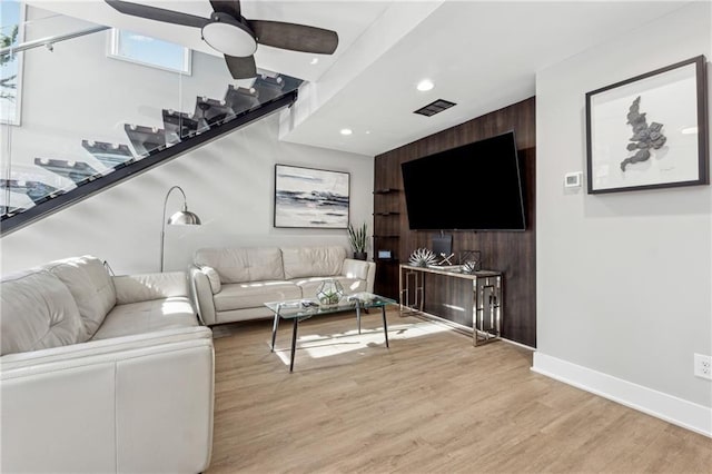 living room with ceiling fan, light wood-type flooring, and wood walls