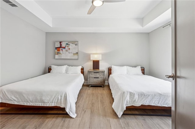 bedroom featuring ceiling fan, a raised ceiling, and light hardwood / wood-style floors