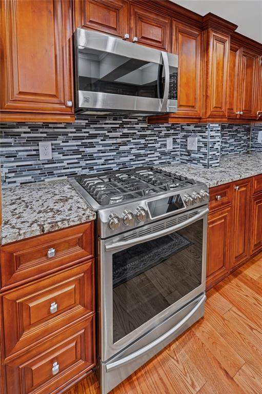 14270 Morning Mountain Way, Milton, GA 30004 - kitchen with stainless steel appliances, tasteful backsplash, light stone countertops, brown cabinetry, and light wood-style floors