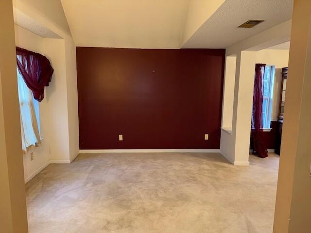 spare room with a textured ceiling, light carpet, and vaulted ceiling