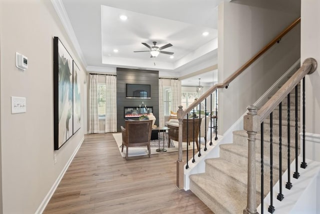 staircase with a large fireplace, ornamental molding, a raised ceiling, hardwood / wood-style flooring, and ceiling fan