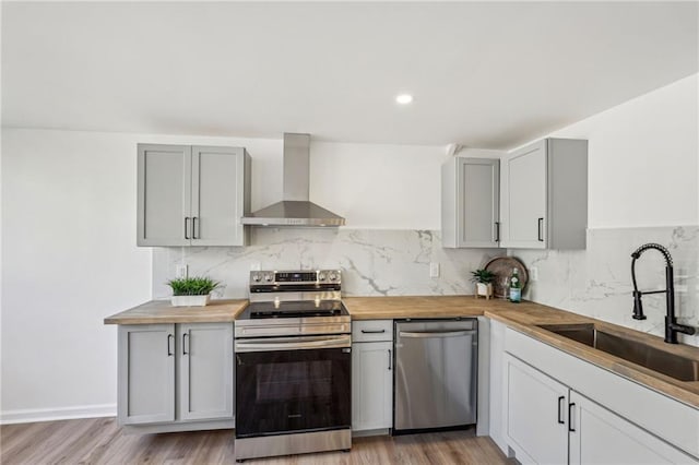 kitchen featuring butcher block countertops, sink, light hardwood / wood-style flooring, appliances with stainless steel finishes, and wall chimney exhaust hood