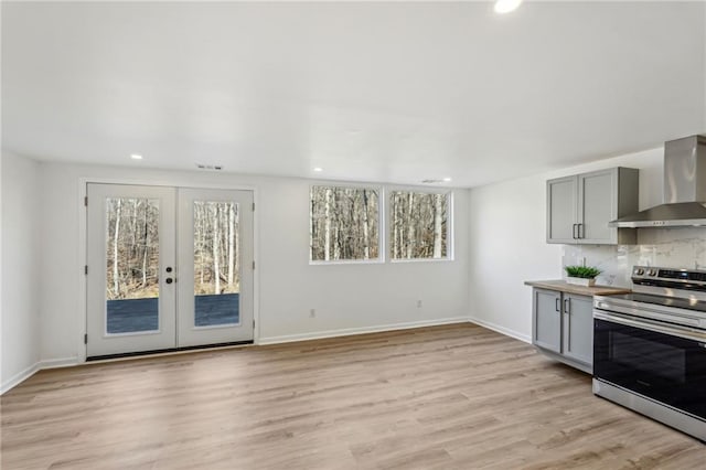 kitchen with gray cabinetry, wall chimney exhaust hood, stainless steel range with electric cooktop, and plenty of natural light