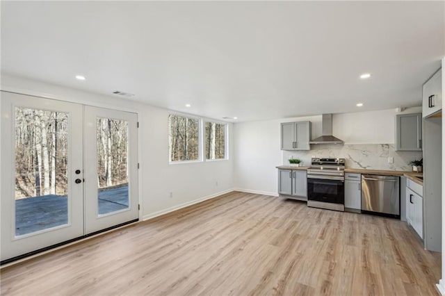 kitchen with tasteful backsplash, light hardwood / wood-style flooring, appliances with stainless steel finishes, gray cabinets, and wall chimney range hood