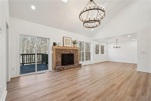 unfurnished living room featuring an inviting chandelier, a fireplace, high vaulted ceiling, and light hardwood / wood-style flooring