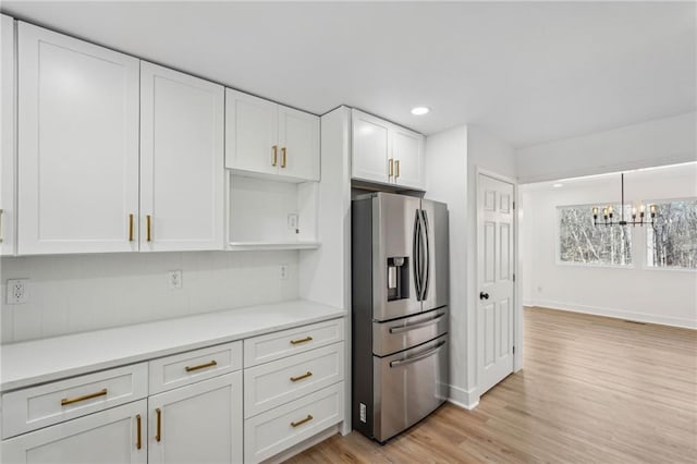 kitchen with pendant lighting, light hardwood / wood-style flooring, stainless steel fridge, an inviting chandelier, and white cabinets