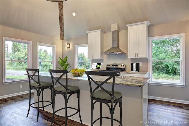 kitchen with stainless steel range with electric cooktop, white cabinets, wall chimney exhaust hood, an island with sink, and a breakfast bar