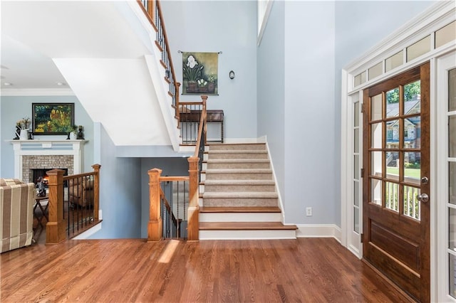 foyer with hardwood / wood-style floors, a brick fireplace, ornamental molding, and a high ceiling