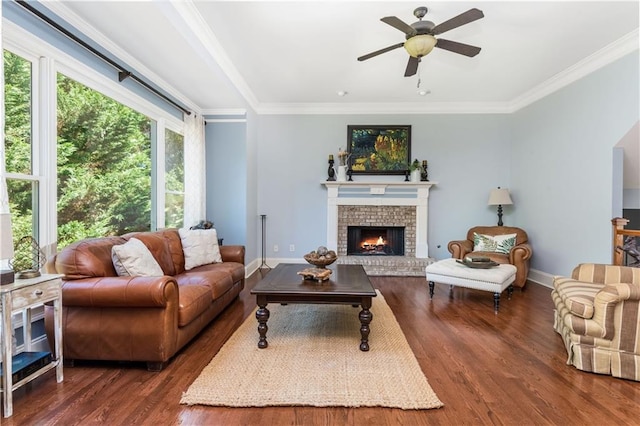 living room with a brick fireplace, crown molding, ceiling fan, and dark wood-type flooring