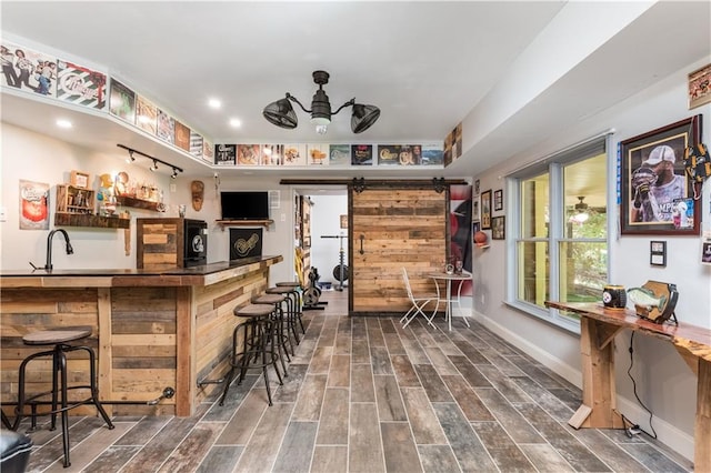 bar featuring a barn door, ceiling fan, and dark wood-type flooring