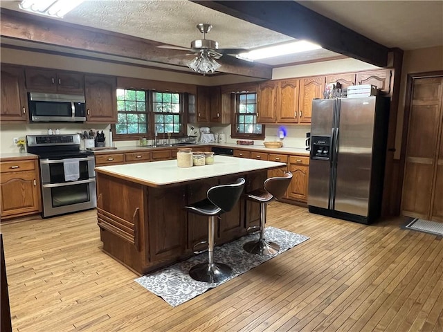 6245 Bannister Rd, Cumming, GA 30028 - kitchen featuring a breakfast bar area, light countertops, appliances with stainless steel finishes, a kitchen island, and light wood-type flooring