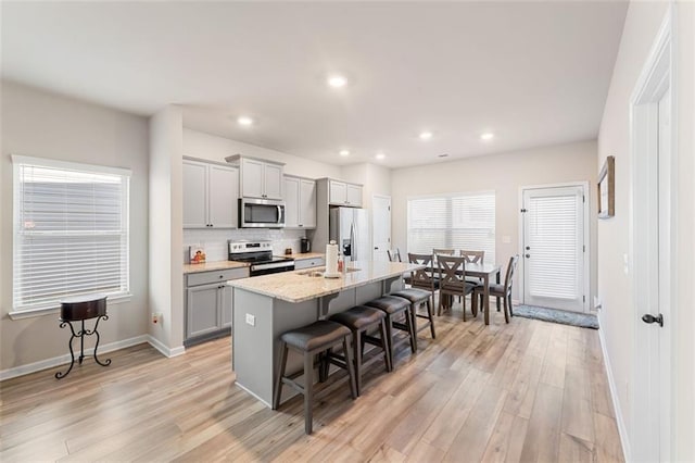 kitchen with a center island with sink, a breakfast bar, gray cabinets, stainless steel appliances, and light hardwood / wood-style floors