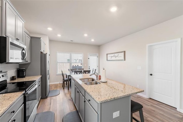 kitchen featuring a kitchen island with sink, stainless steel appliances, sink, light wood-type flooring, and gray cabinets