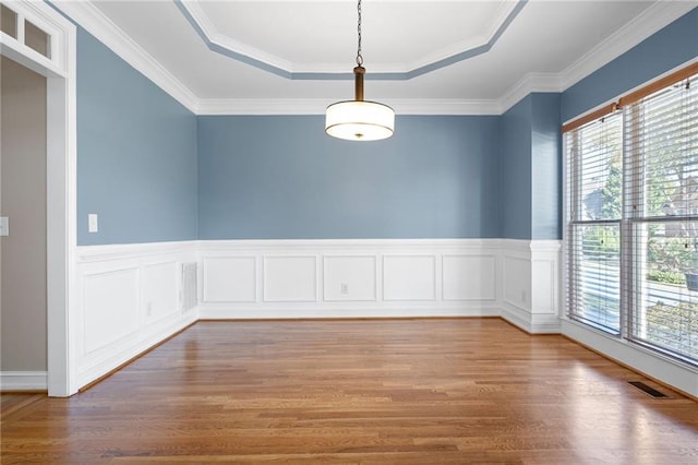 spare room with a healthy amount of sunlight, ornamental molding, a tray ceiling, and hardwood / wood-style floors