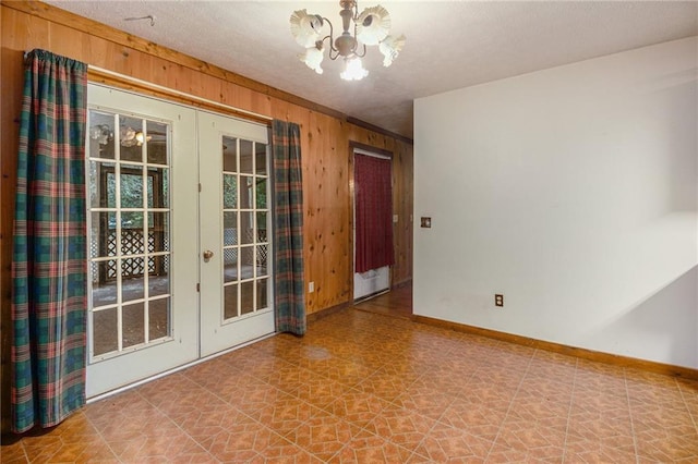 spare room featuring a textured ceiling, french doors, a chandelier, and wood walls