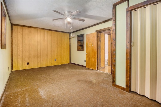 empty room with crown molding, ceiling fan, a textured ceiling, and wood walls