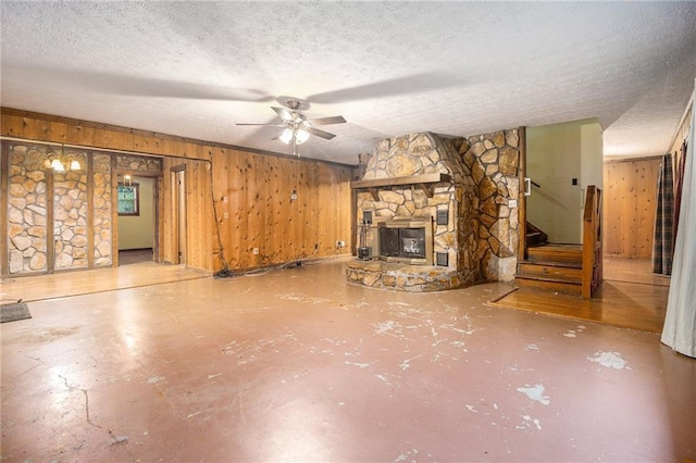 unfurnished living room featuring ceiling fan, a fireplace, a textured ceiling, and wood walls