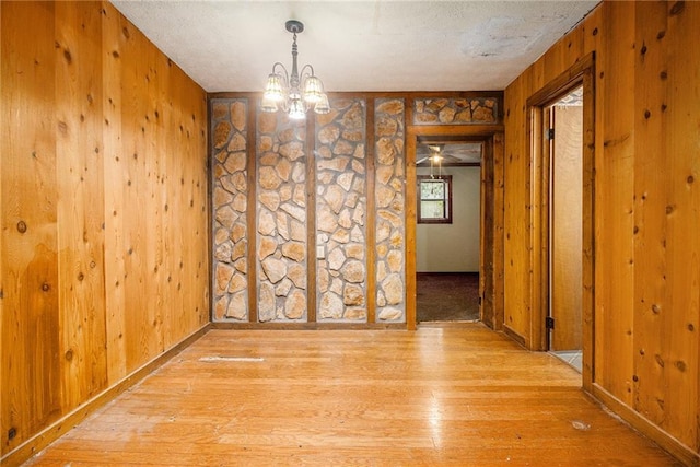 unfurnished dining area with an inviting chandelier, light hardwood / wood-style floors, and wood walls