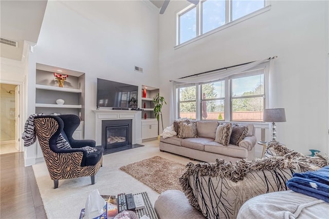 living room featuring built in features, visible vents, a fireplace with flush hearth, and a wealth of natural light