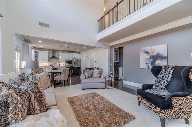 living area with baseboards, visible vents, recessed lighting, a towering ceiling, and crown molding