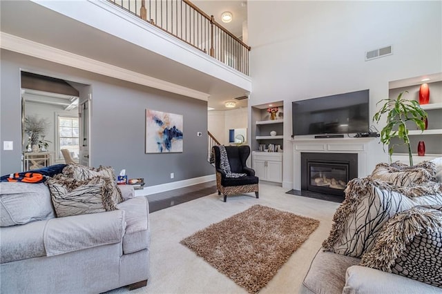 carpeted living room with visible vents, crown molding, baseboards, a fireplace with flush hearth, and built in features