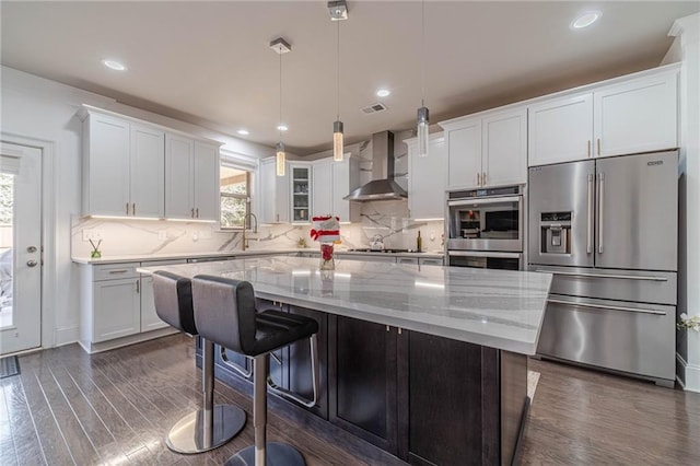 kitchen featuring a kitchen island, dark wood finished floors, stainless steel appliances, white cabinets, and wall chimney exhaust hood