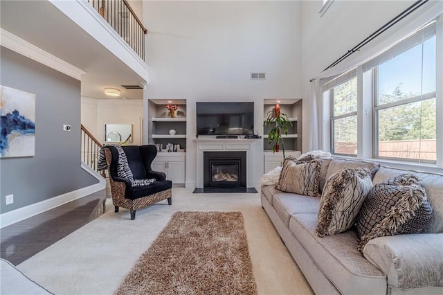 living room with stairway, built in features, baseboards, visible vents, and a fireplace with flush hearth