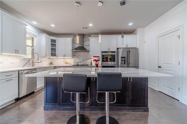 kitchen with a kitchen island, stainless steel appliances, white cabinets, a kitchen bar, and wall chimney exhaust hood