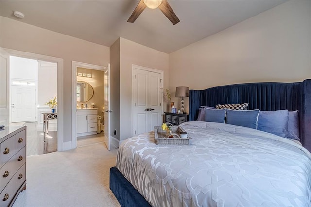 bedroom featuring baseboards, light carpet, a closet, ensuite bath, and a ceiling fan