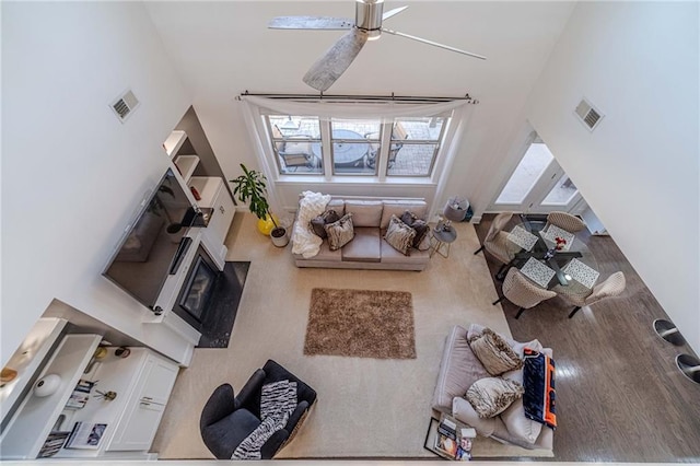 living room featuring visible vents, wood finished floors, a ceiling fan, and a towering ceiling