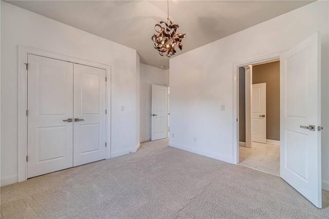 unfurnished bedroom with a notable chandelier, baseboards, a closet, and light carpet