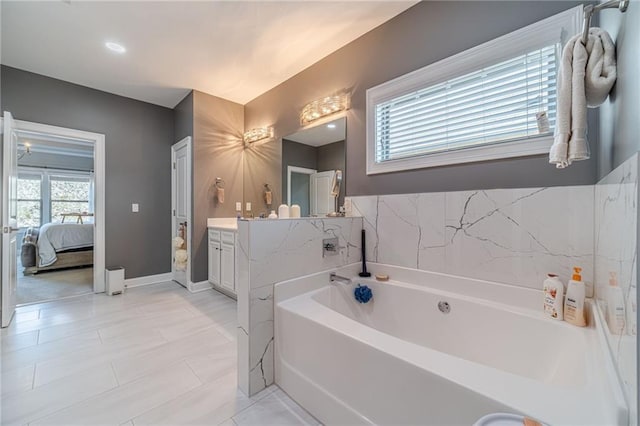 ensuite bathroom with a bath, vanity, ensuite bath, and baseboards