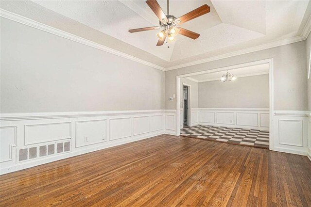 spare room featuring ceiling fan with notable chandelier, a tray ceiling, dark wood-type flooring, and crown molding